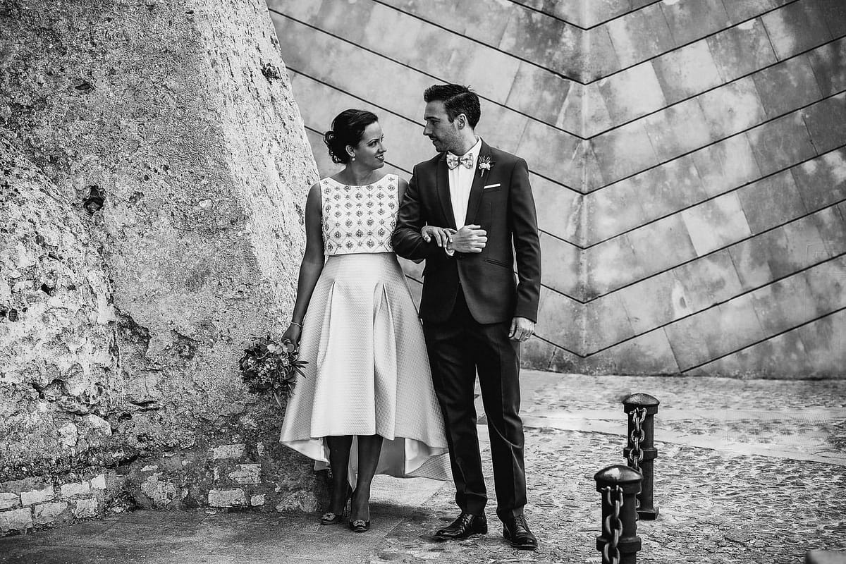 post-wedding photographic portrait of a newly married couple walking arm in arm and looking at each other in the streets of the wall of dalt vila in professional photography in ibiza