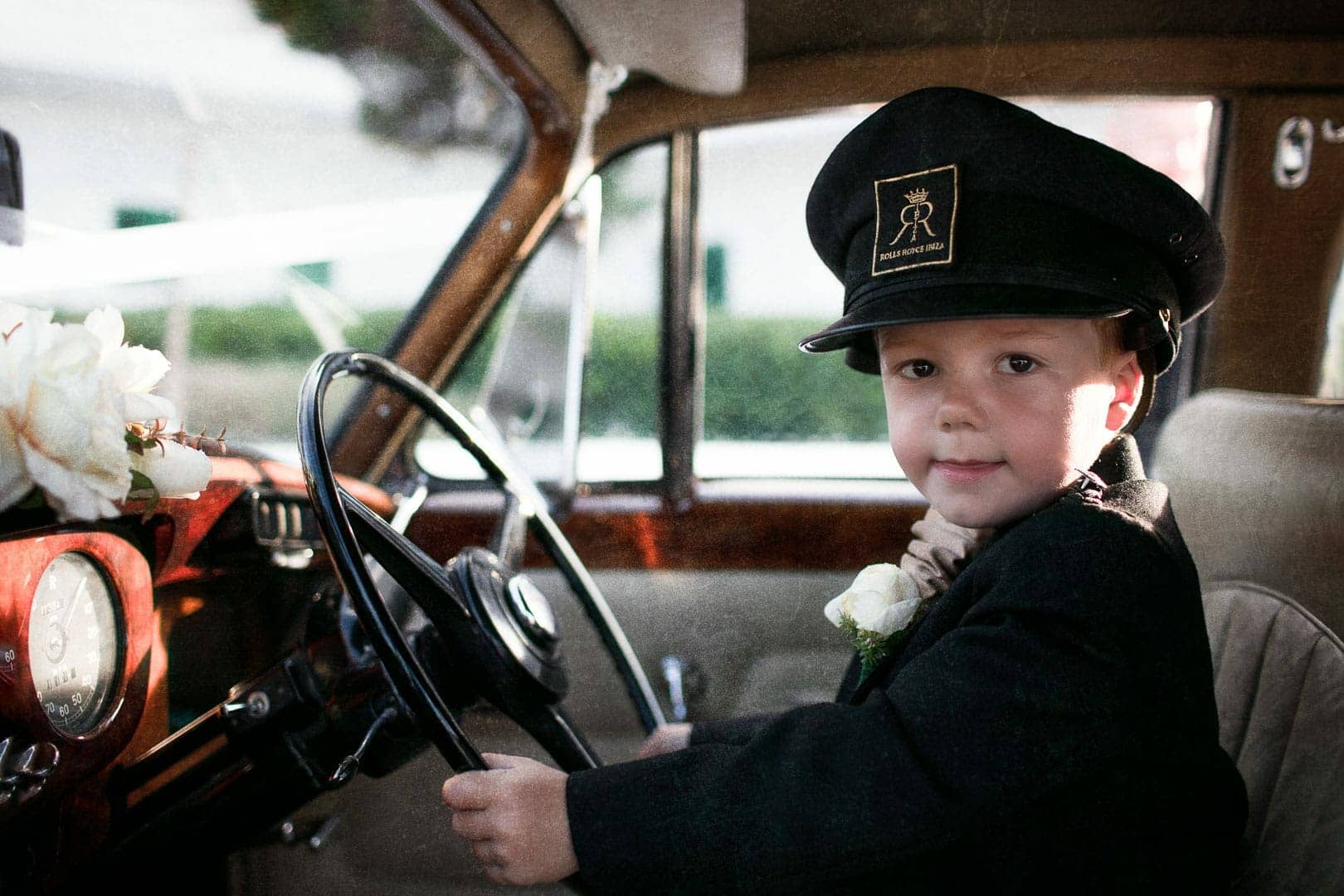 snapshot of a boy sitting at the wheel of the newlyweds' car with captain's hat and jacket suit in a restaurant in cala de bou in wedding photographer in Ibiza