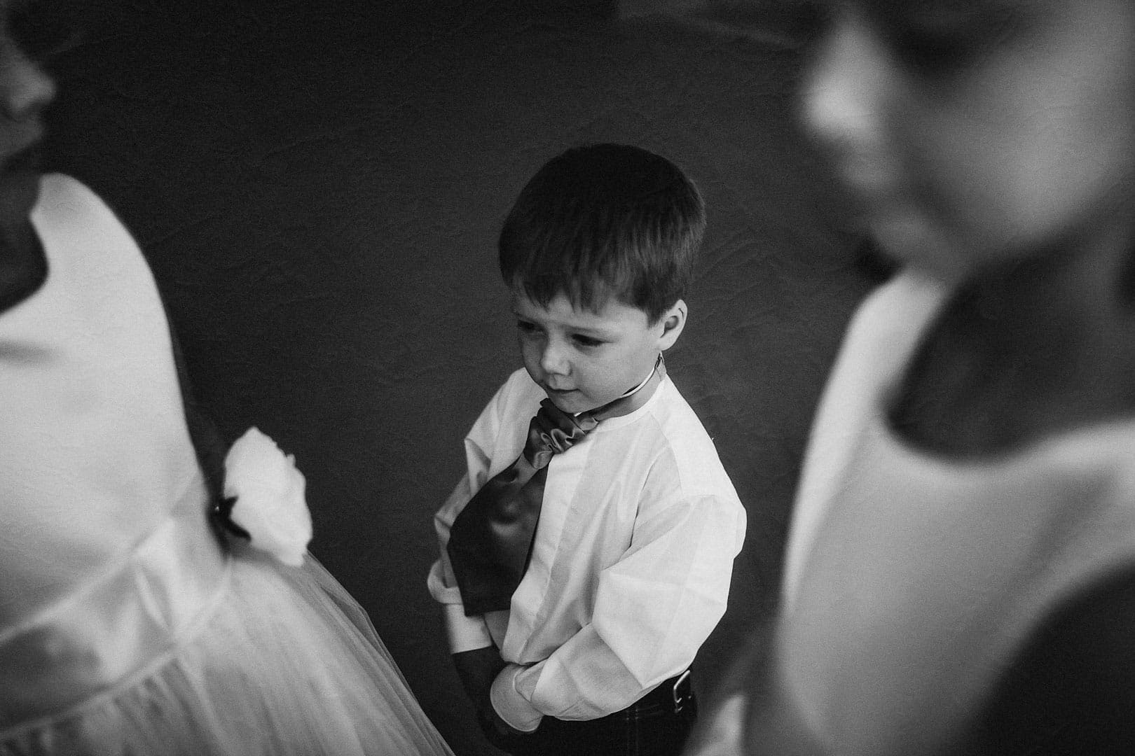 instant black and white portrait of the son of the bride and groom with bow tie and blouse around his cousins in Ibiza wedding photographer