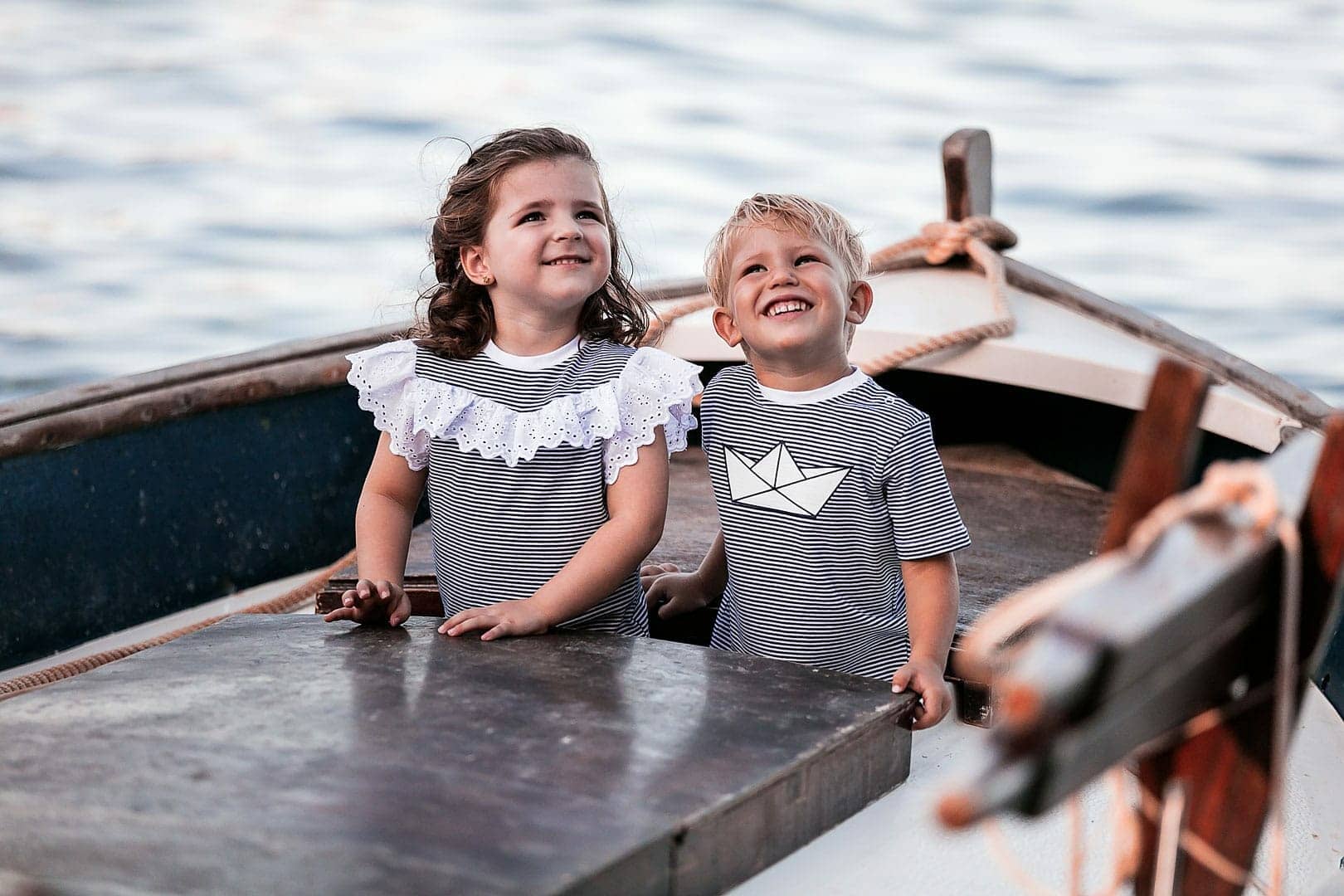 fotografía de dos niños sonrientes jugando sobre una barca vestidos con camiseta rayada de color azul en embarcadero de Ibiza