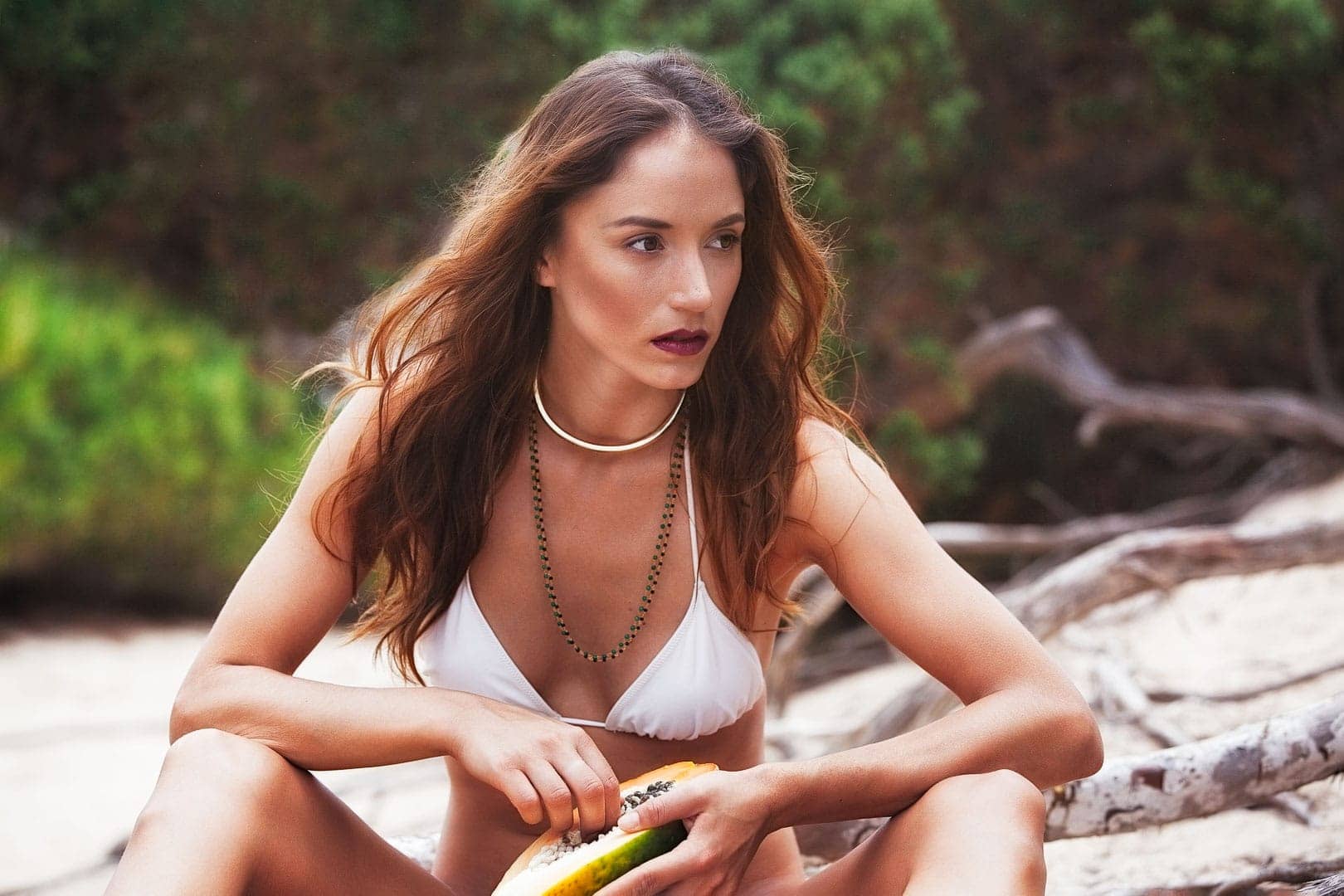 fotografia de modelo posando para marca de bikini jugando con un fruto exotico sentada en las playas de salinas de ibiza