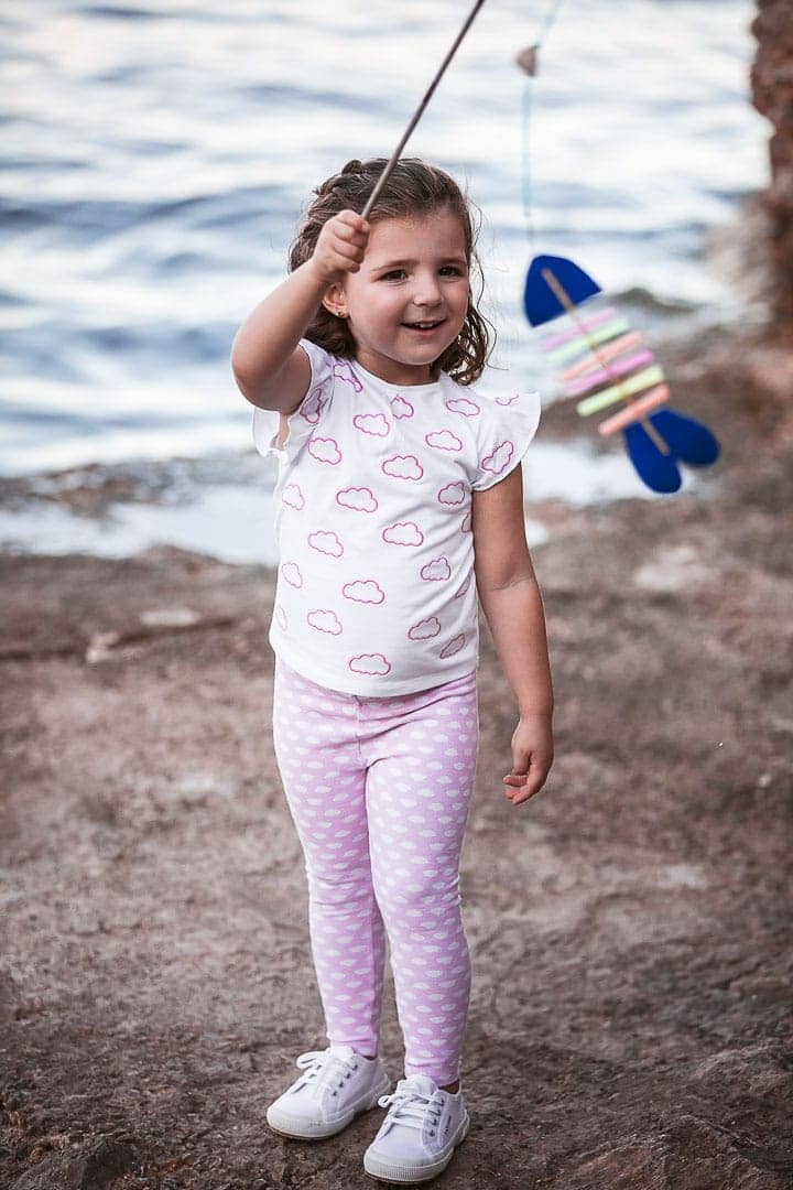 Reportaje fotográfico de ropa infantil con niña vestida con pantalón pitillo y camiseta rosada jugando en embarcadero de Ibiza