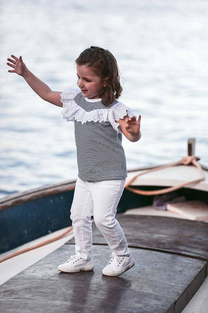 photo of a smiling girl playing on a boat dressed in a blue striped T-shirt and white pants on a pier in Ibiza