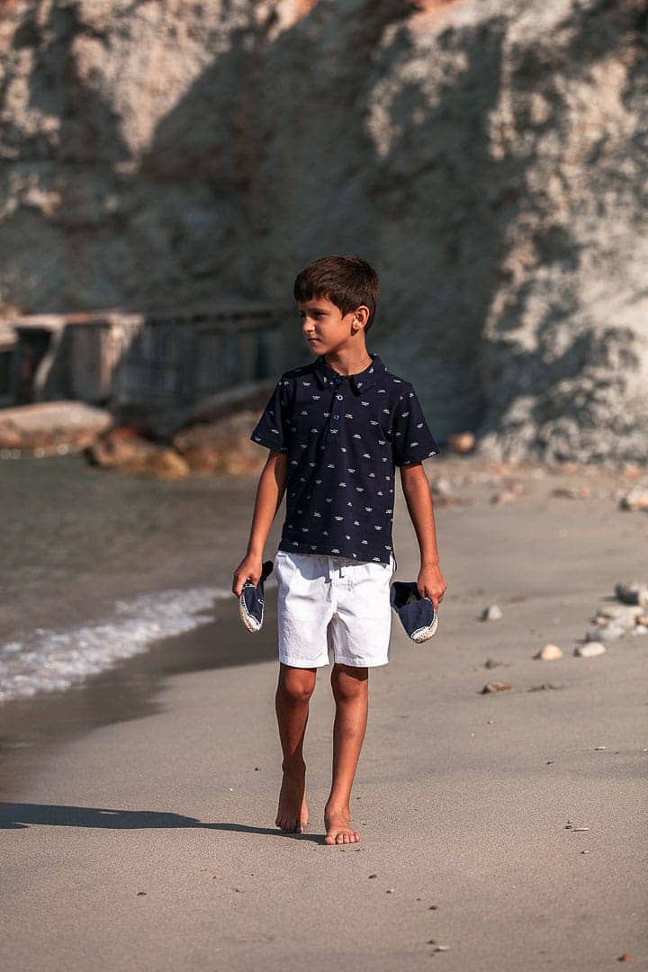 Reportaje fotográfico de ropa infantil con niño caminando en la orilla de la playa de cala Dort en Ibiza