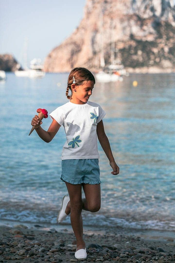 Fotografía de niña jugando en la orilla del mar vestida con ropa de verano
