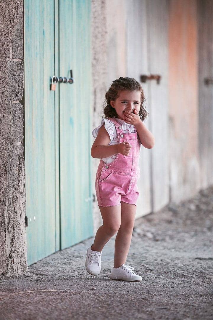 Reportaje fotográfico de ropa infantil con niña vestida con peto rosado jugando en embarcadero de Ibiza