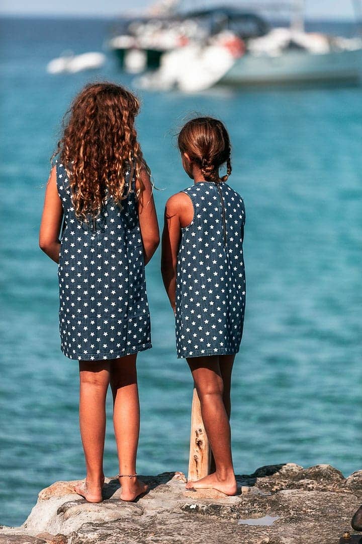 Retrato de dos niñas posando con ropa de marca infantil con el mismo vestido baquero en estampado de estrellas mirando al mar
