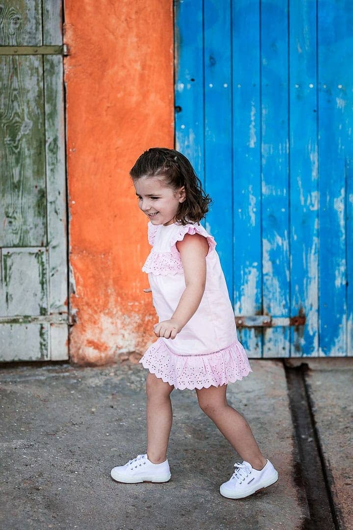 Reportaje fotográfico de ropa infantil con niña vestida con vestido rosado jugando en embarcadero de Ibiza